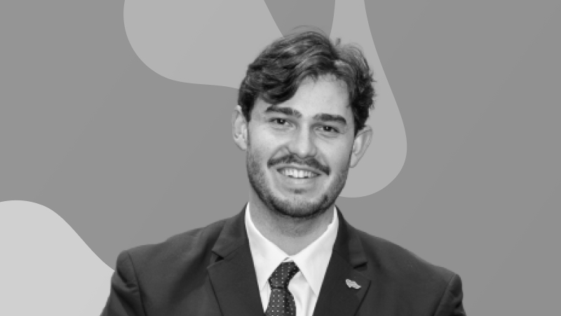 Retrato a preto e branco de um homem de fato e gravata a sorrir, sobre fundo gráfico abstrato.