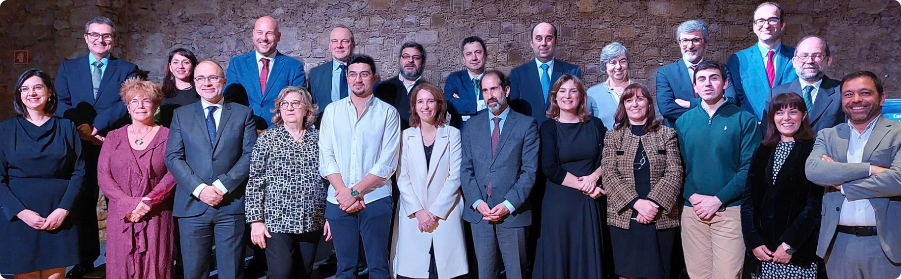 Fotografia de grupo dos membros do conselho do CNIPES durante um evento institucional junto a uma parede de pedra.